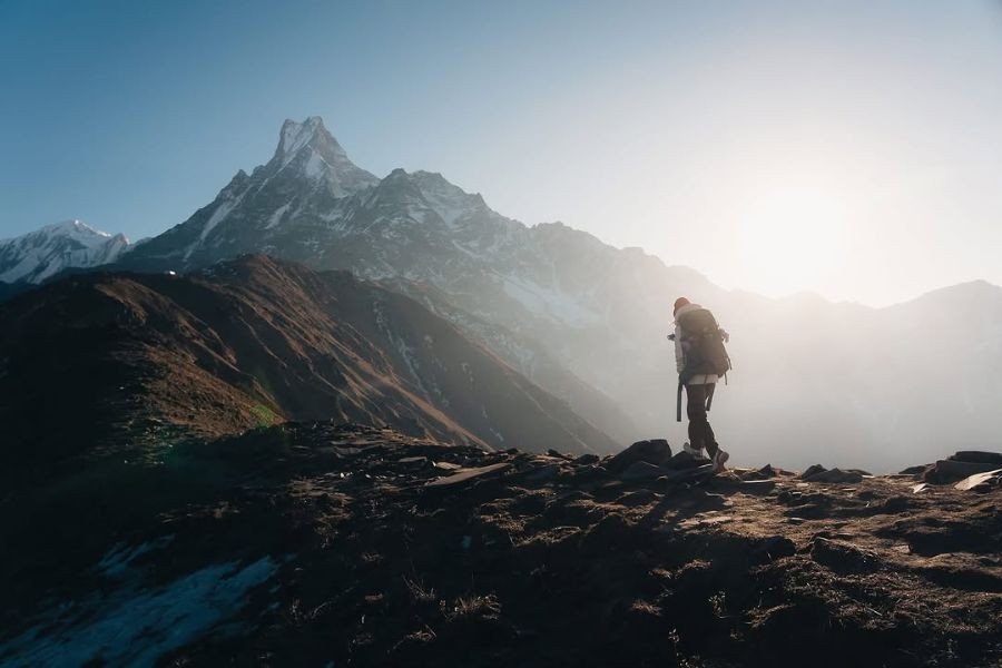 Solo trekker hiking at sunrise beneath the dramatic Machhapuchhre peak.